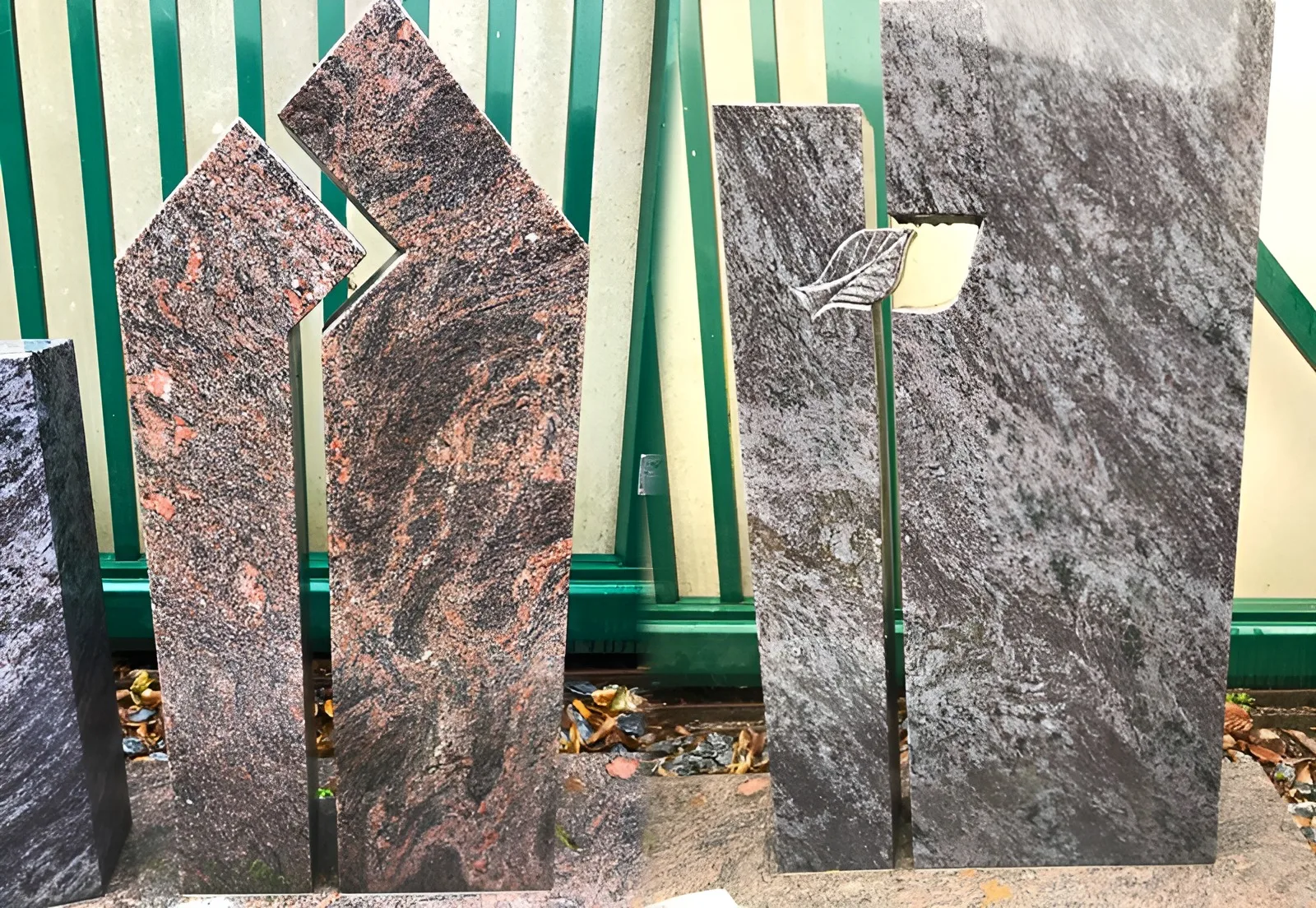 Moderne Grabmale aus Granit in der Ausstellung: zwei ineinandergreifende rötlich gemaserte Stelen und ein grauer Stein mit Blattornament